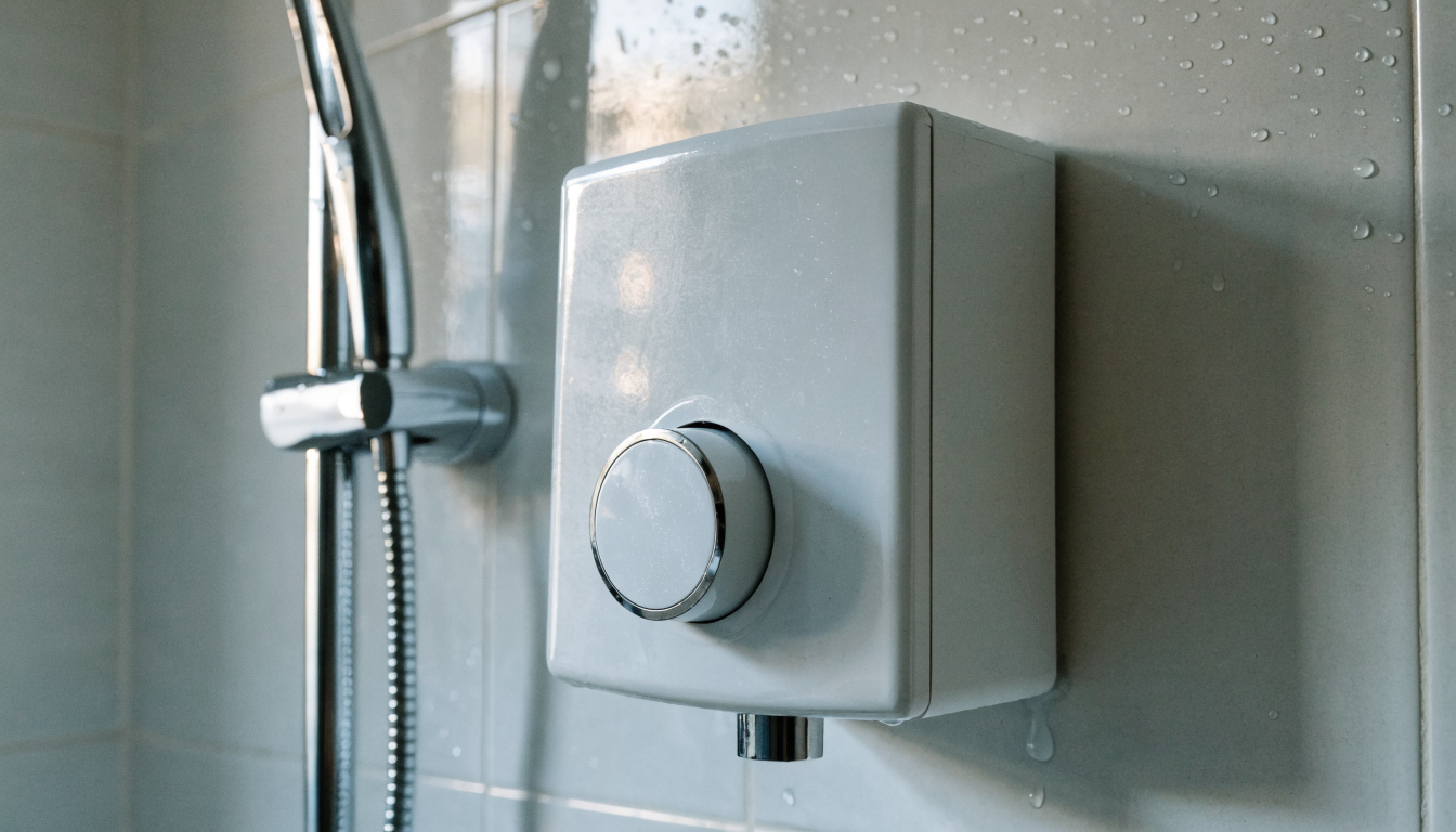 A white electric shower unit mounted on a tiled bathroom wall with the riser rail and handset beside it