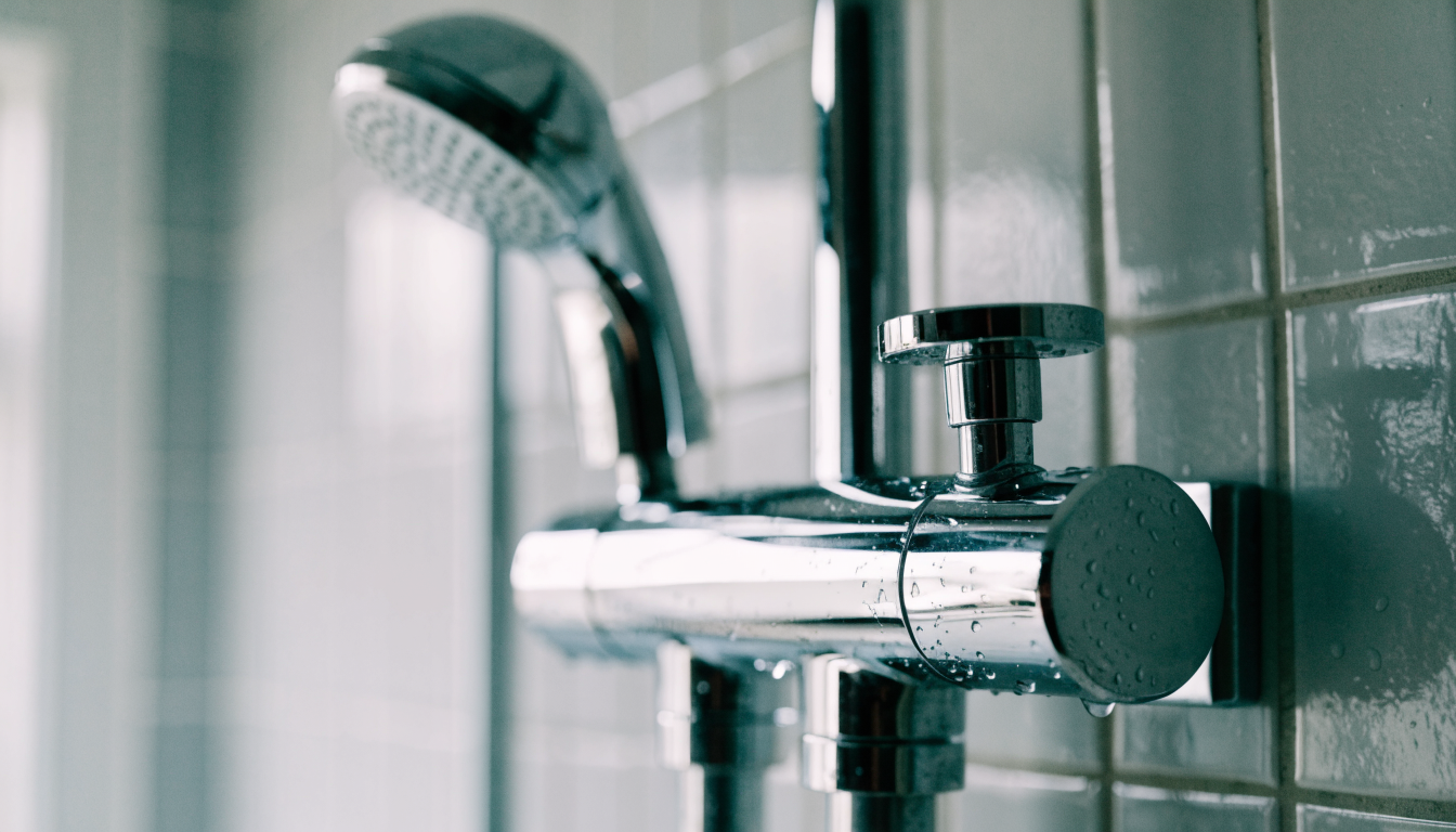 A chrome thermostatic bar mixer shower mounted on a tiled bathroom wall, with the handset and riser rail behind